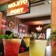 Two cocktails with fruit in front of Mojito Port sign