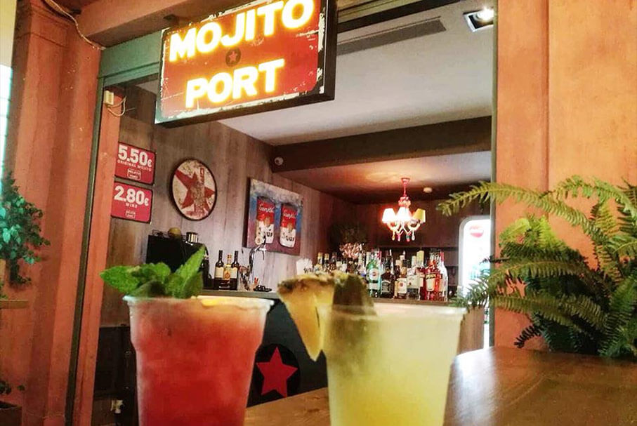 Two cocktails with fruit in front of Mojito Port sign
