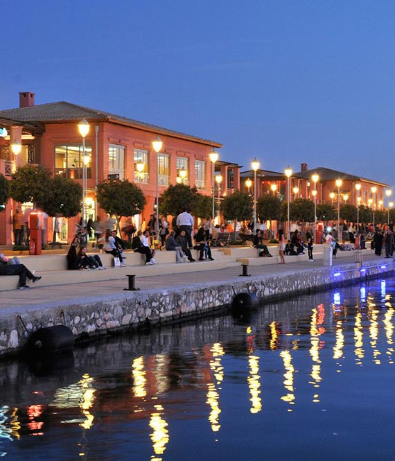 Promenade with people in front of Flisvos Marina, Athens buildings at dusk