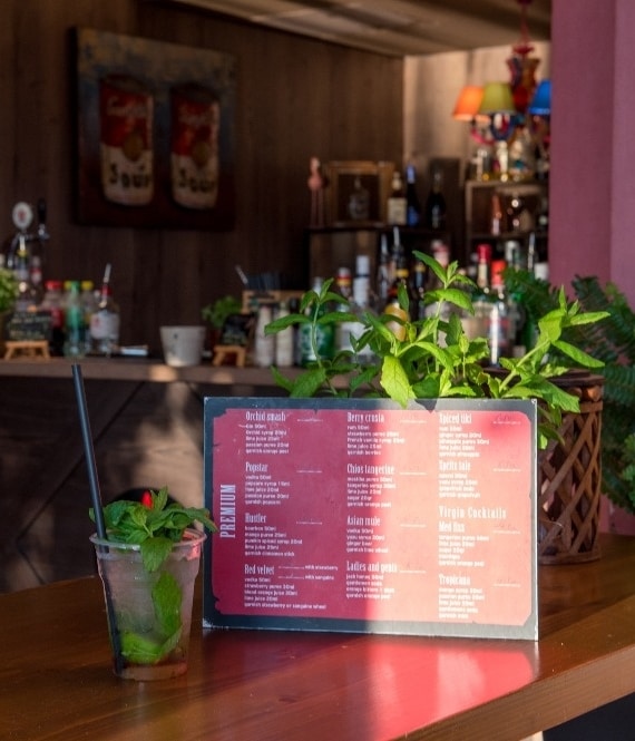 Mojito in plastic cup in front of fully stocked bar and drink menu