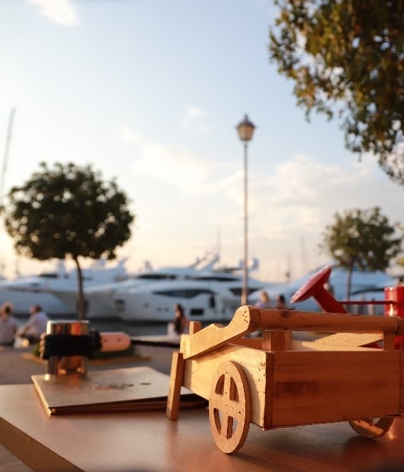 Wooden toy car on table facing yachts