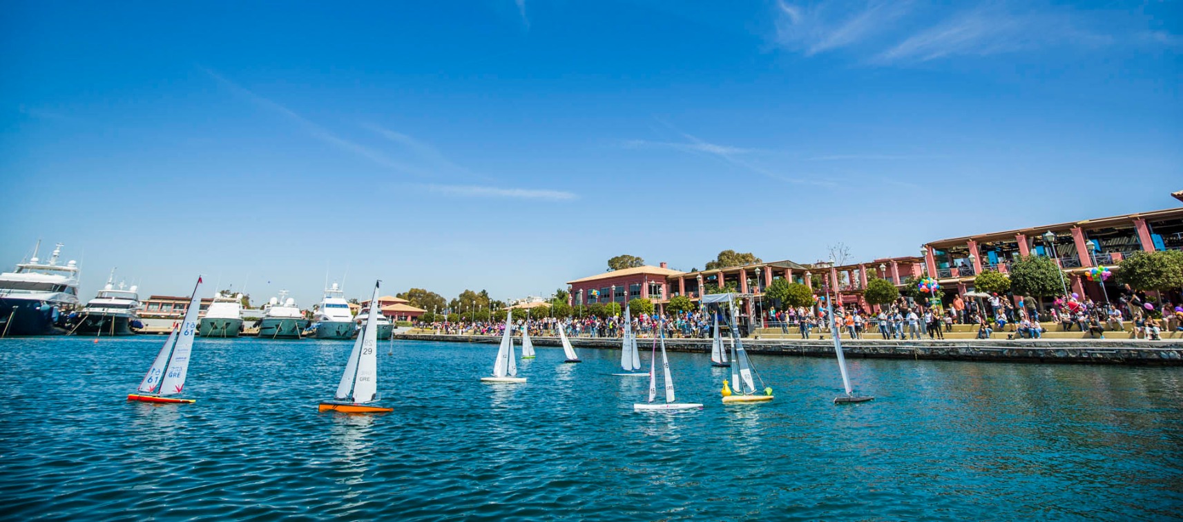 Toy sailboats racing in sea in front of yachts